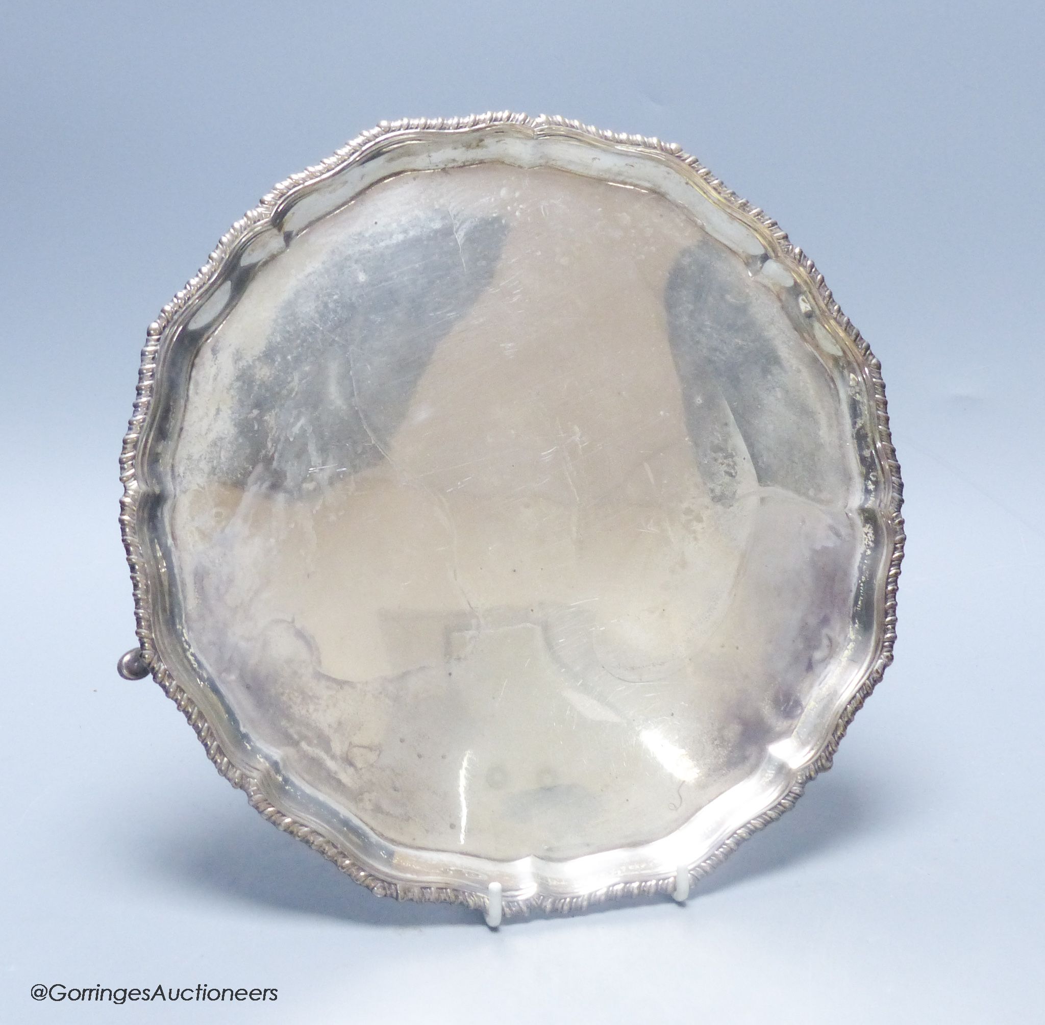 A circular silver salver with shaped gadrooned edge, on three hoof feet, 14.79oz